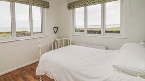 Un dormitorio con una cama grande, dos ventanas con cortinas, un adorno con forma de corazón y vista al mar.