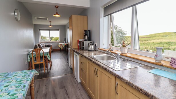 A kitchen with wooden cabinets, a granite countertop, and a window with a view of a green landscape. - Budle Bay Cottage (Bamburgh)