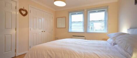 A bedroom with a bed, white walls, a ceiling light, and a window with blinds.