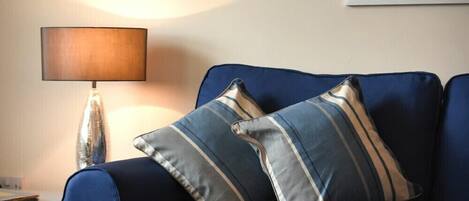 Un sofá azul con almohadones a rayas, una lámpara y un cuadro en la pared.