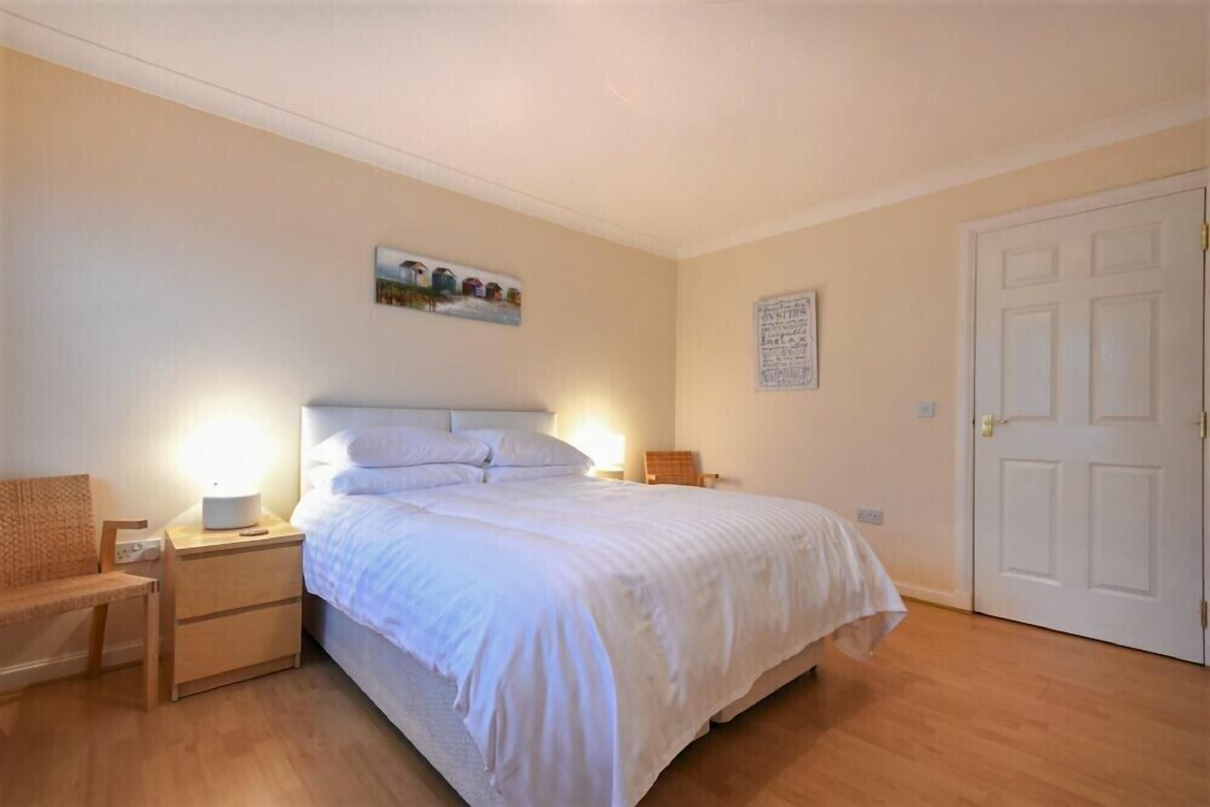 Een slaapkamer met een bed, nachtkastjes, een stoel, een deur en wanddecoratie.