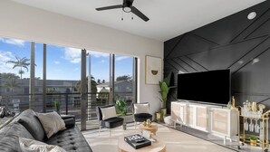 Ein modernes Wohnzimmer mit Sofa, Couchtisch, Fernseher und einem Balkon mit großen Fenstern.