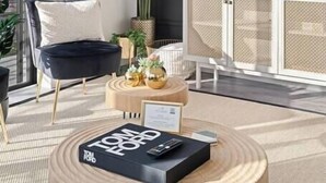Ein modernes Wohnzimmer mit einem großen Flachbildfernseher, einem runden Couchtisch aus Holz, einem schwarzen Sofa und einer üppigen Pflanze im Topf.