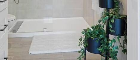 A modern bathroom with a shower, a bathtub, a towel rack, and a potted plant.