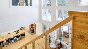 Um loft espaçoso com pé direito alto, grandes janelas, escada de madeira e área de jantar com lareira.