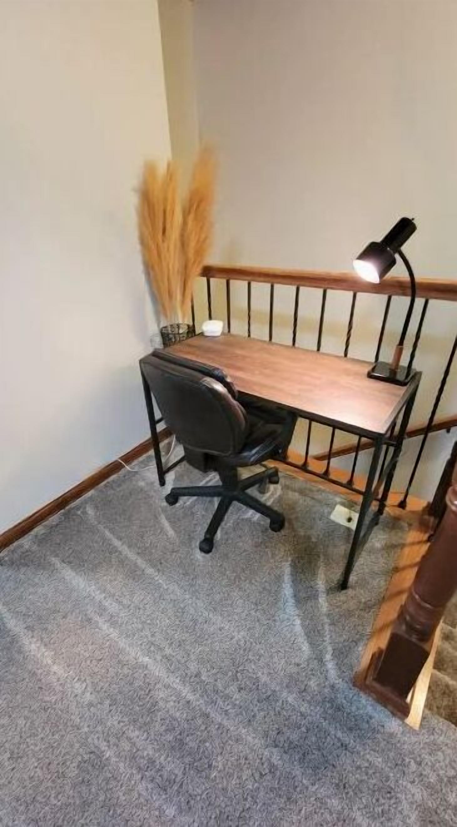 Un pequeño espacio de oficina con un escritorio de madera, una silla de oficina negra, una lámpara y una planta decorativa.