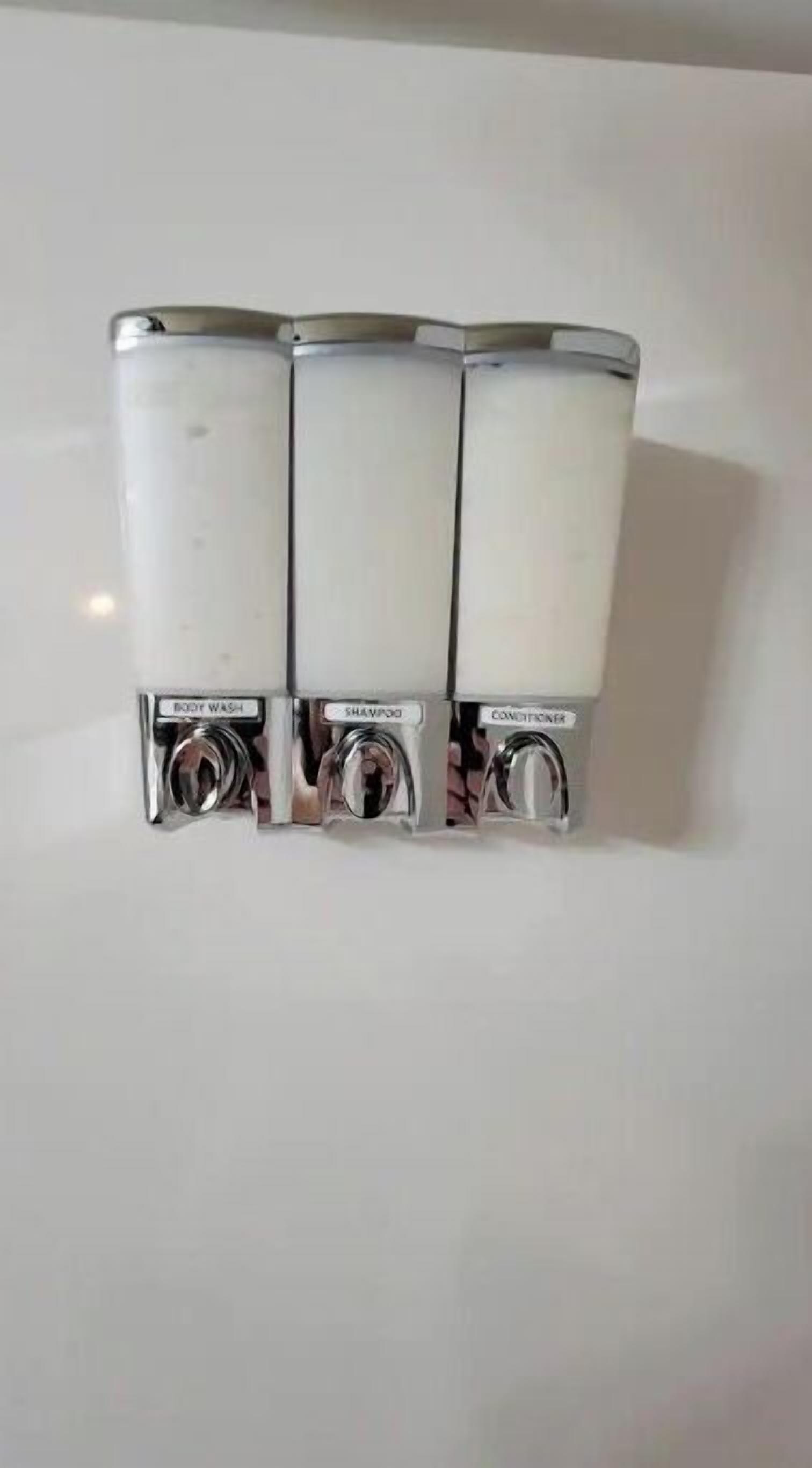 A set of three white dispensers with labels for body wash, shampoo, and conditioner.