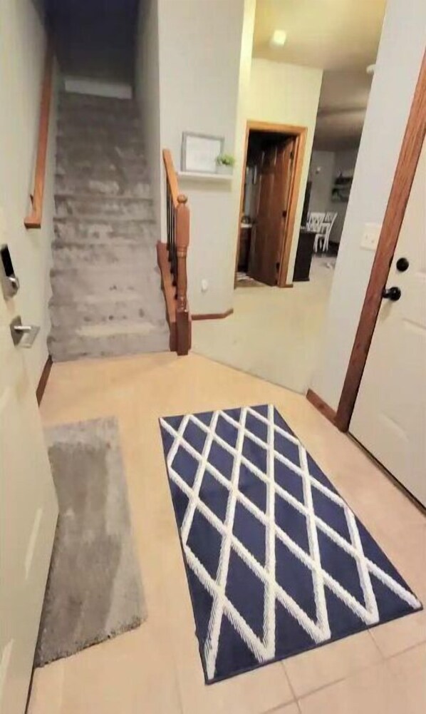 A hallway with a wooden staircase, a patterned rug, and a door leading to another room.