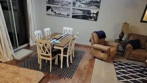 Een zithoek met een houten tafel en stoelen, een bank en een vloerkleed met dessin.