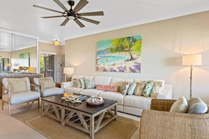 A living room with a white sofa, two armchairs, a coffee table, and a painting of a beach scene.