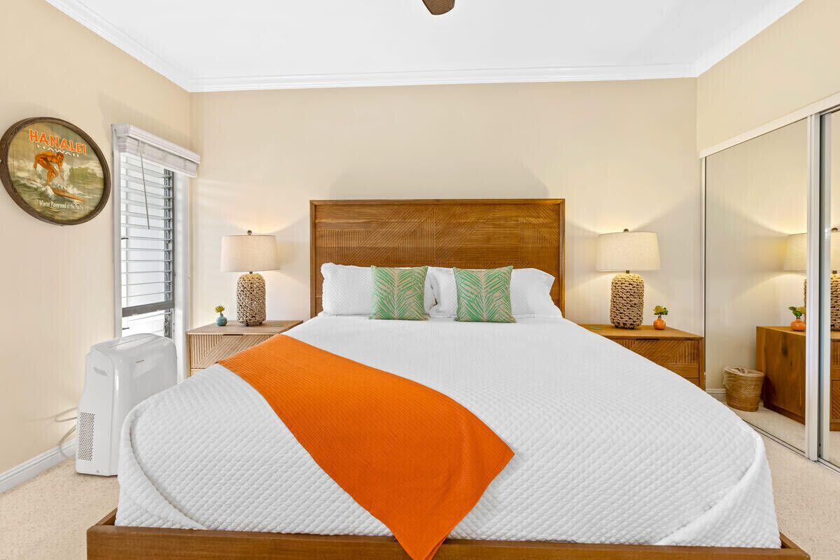 A hotel room with a large bed, two bedside lamps, a wooden headboard, a mirror, and a window with blinds.