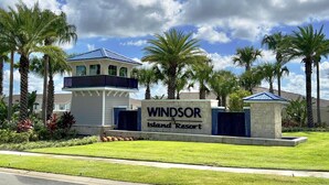 A sign for Windsor Island Resort with a two-story building and a balcony, surrounded by palm trees and a well-maintained lawn.