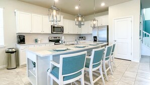 A modern kitchen with white cabinets, stainless steel appliances, a central island with bar seating, and pendant lighting.