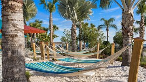 A hammock set up on a sandy beach with palm trees in the background.