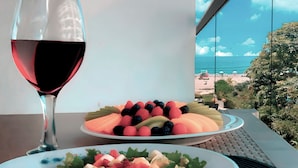 Una mesa con una copa de vino tinto, un plato de frutas variadas y una ensalada.