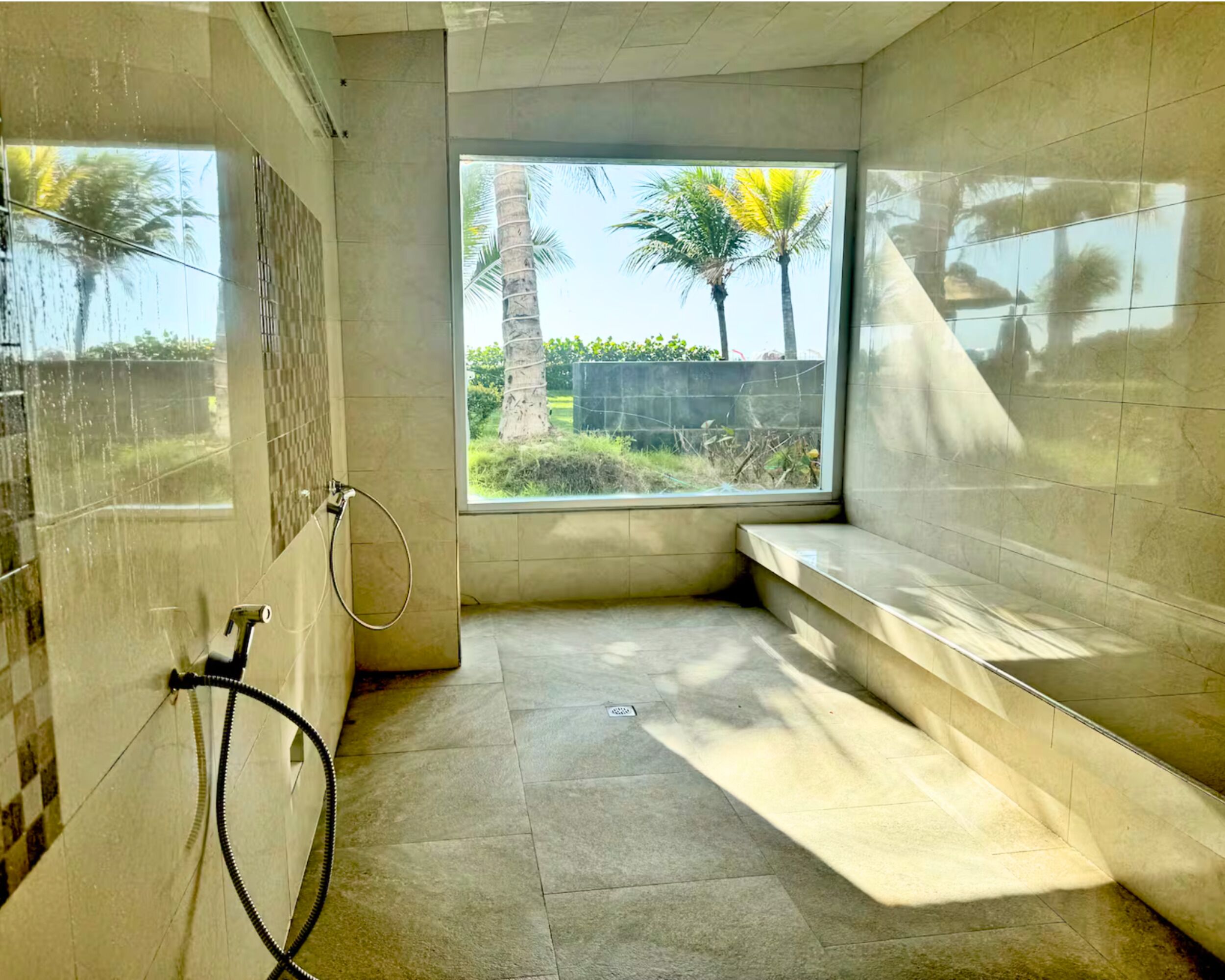 Un baño con un ventanal grande, un perchero para toallas y un banco.