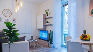 Un soggiorno moderno con una televisione a schermo piatto, un tavolo da pranzo con sedie, una pianta in vaso e un cactus.