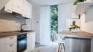 Una cucina moderna con mobili bianchi, un piano di lavoro in legno e un forno integrato. Si nota una piccola isola con un cesto di frutta e una sedia.