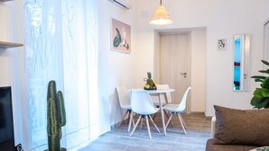 Un soggiorno moderno con una televisione a schermo piatto, un cactus, un'area pranzo con tavolo e sedie, e un divano con cuscini.