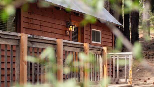 A wooden cabin with a metal roof, a wooden deck, and a small porch. - Lakeshore Resort (Lakeshore)