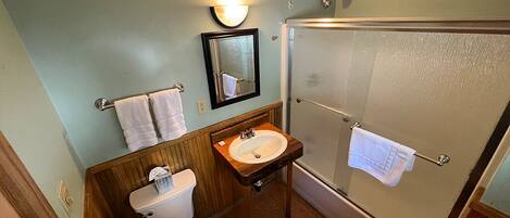 A bathroom with a toilet, sink, mirror, and glass shower stall.