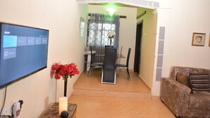 Un salon avec un téléviseur, une table entourée de chaises, un vase rempli de fleurs et un canapé.