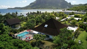 A residential area with a swimming pool, a large house with a dark roof, and a view of a mountain and the sea. - Unique luxuous 350sq m Villa with pool, fitness area, home cinema lounge .... (bora bora)