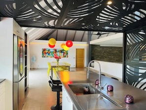 A modern kitchen with a central island, a sink, and a dining area with yellow chairs. - Unique luxuous 350sq m Villa with pool, fitness area, home cinema lounge .... (bora bora)