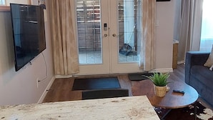 A modern living room with a large wooden table, a sofa, a TV mounted on the wall, and a sliding glass door leading to a balcony. - Cozy basement suite near the mountains (Cochrane)