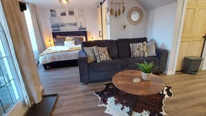 A cozy living room with a sofa, a coffee table, and a bed with a headboard. - Cozy basement suite near the mountains (Cochrane)