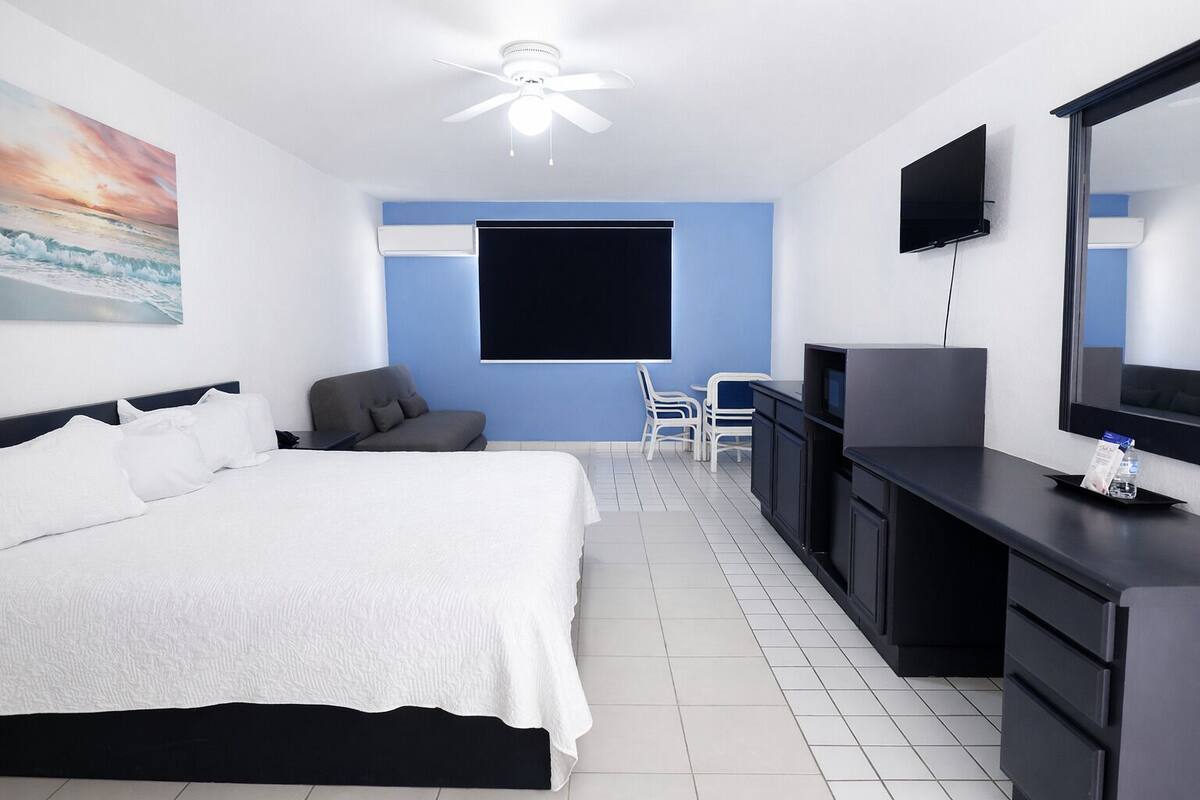 A hotel room with a bed, a desk, a chair, a television, and a ceiling fan.