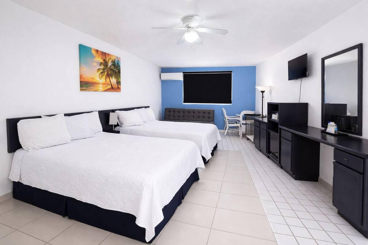A hotel room with two beds, a desk, a chair, a television, and a ceiling fan.