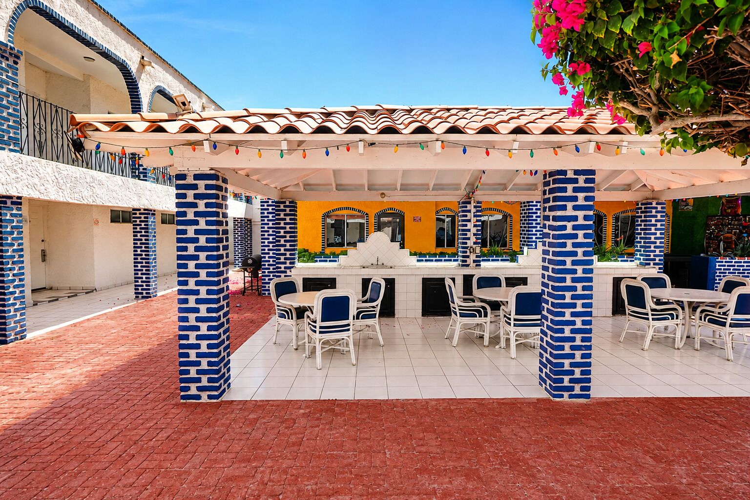 An outdoor patio area with brick columns, white chairs, and a tiled floor.
