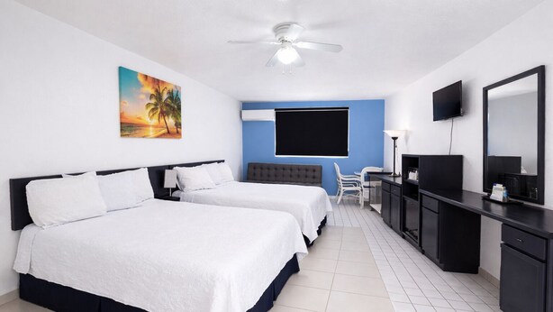 Une chambre d’hôtel avec deux lits, un bureau, une chaise, une télévision et un ventilateur de plafond.