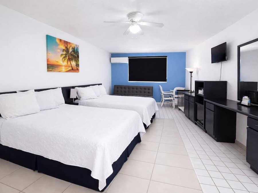 A hotel room with two beds, a desk, a chair, a television, and a ceiling fan.