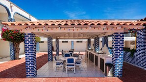 Une terrasse extérieure dotée d’un sol carrelé, de colonnes en briques bleues et blanches, d’un espace salon couvert et d’un bar.