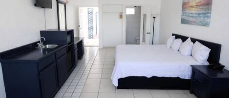 A hotel room with a bed, a desk with a sink, a television, and a painting on the wall.