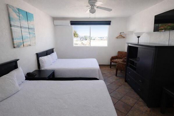 A hotel room with two beds, a desk, a chair, a TV, and a window with a view.