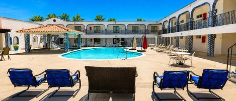 A pool area with lounge chairs and a building with a tiled roof.