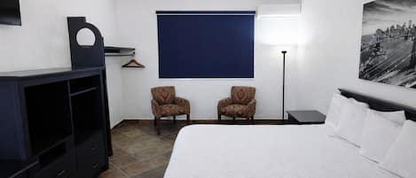 Habitación de hotel con cama, dos sillones, televisión, escritorio y un cuadro en la pared.