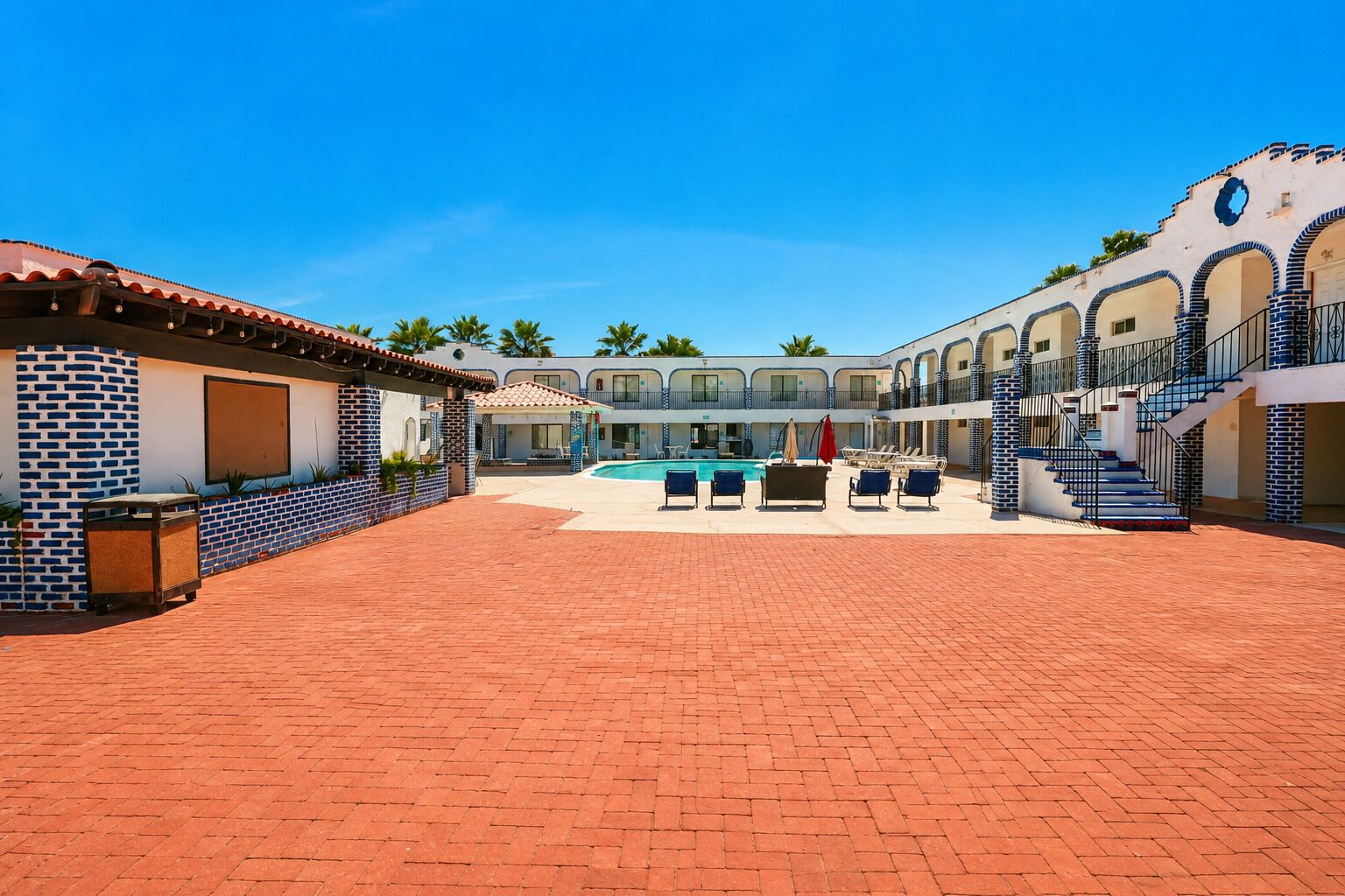 A hotel courtyard with a swimming pool, lounge chairs, and a covered seating area.