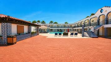 A hotel courtyard with a swimming pool, lounge chairs, and a covered seating area.