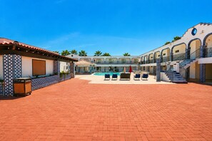 A hotel courtyard with a swimming pool, lounge chairs, and a covered seating area.