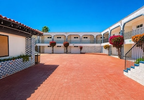 A courtyard with a brick floor, white walls, and blue accents. There are potted plants and a staircase with blue steps. - Playa Inn Rocky Point (Puerto Peñasco)
