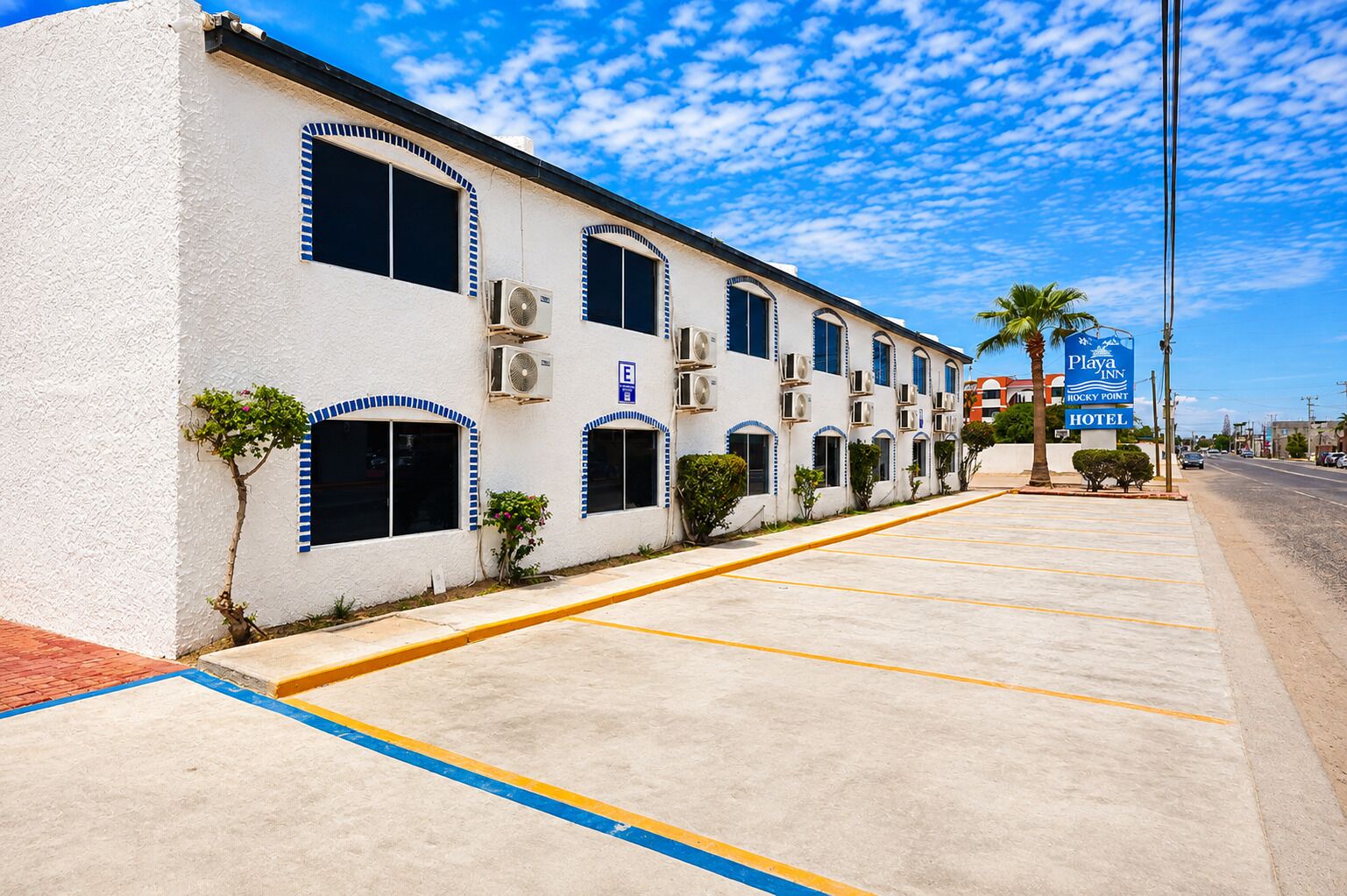 A hotel with a row of rooms, air conditioning units, and a sign for Playa Inn Rocky Point Hotel.