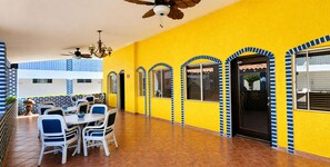 A yellow building with blue and white accents, a covered patio with tables and chairs, and a ceiling fan. - Playa Inn Rocky Point (Puerto Peñasco)