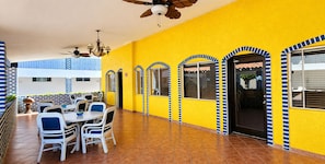 A yellow building with blue and white accents, a covered patio with tables and chairs, and a ceiling fan. - Playa Inn Rocky Point (Puerto Peñasco)