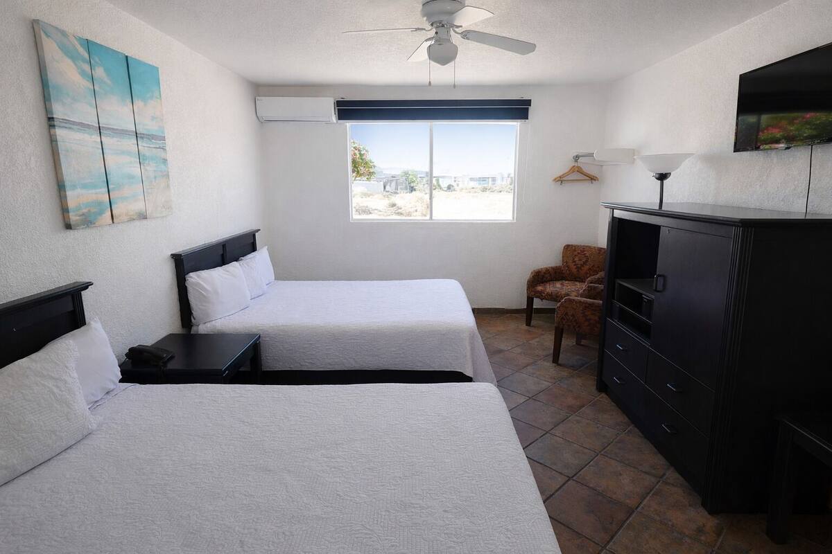 A hotel room with two beds, a desk, a chair, a TV, and a window with a view.