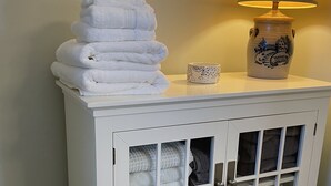 A white cabinet with glass doors containing folded towels and a decorative vase with a lamp on top. - Harbor View Suite
Talbot County License Number STRN-25-58 (Saint Michaels)