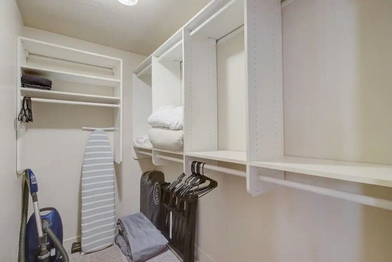 Armário bem organizado com prateleiras, espaço para pendurar roupas e um aspirador de pó.